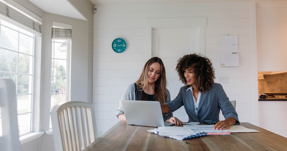 two women looking at website homepage on laptop.